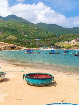 Bai Xep Beach, Vietnam - 30 January 2026: View of turquoise basket boats resting on the golden sand under a bright sky, with lush green mountains in the backdrop.