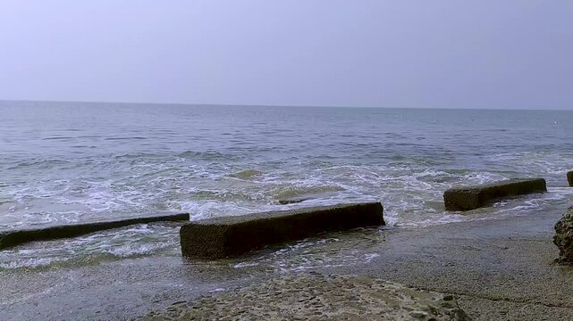 A tranquil coastal scene captured at Digha Sea Beach in West Bengal, India, featuring gentle ocean waves meeting the sandy shoreline. Concrete breakwaters extend into the sea, against the calm horizon