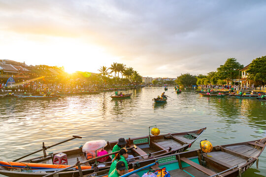 Hoi An, Vietnam - 28 January 2026: View of the lantern-lit bridge reflecting in the tranquil river as boats drift past, bathed in the warm glow of the setting sun.