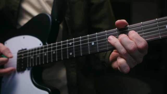 Close up guitarist hands playing chords and solo on fretboard of black and white electric guitar, with other hand strumming strings during musical performance. Musician playing an electric guitar solo