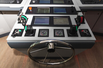 Modern ship bridge console featuring a stainless steel steering wheel, throttle levers, instrument gauges and navigation screens. Professional maritime navigation simulation system for trainings © evannovostro