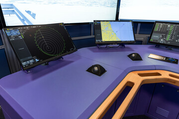 A modern ship simulator bridge, blue navigation console with multiple monitors showing radar and electronic charts, keyboards and control panels used for maritime navigation and vessel monitoring © evannovostro
