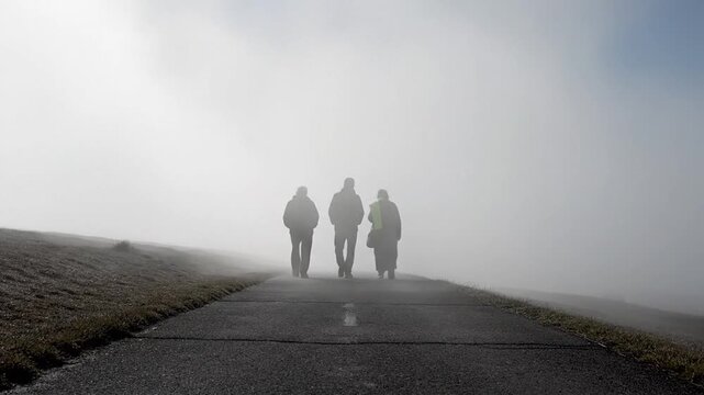 Three people walking away on a foggy road with hoods