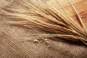 Naklejka premium Wheat stalks placed on burlap fabric next to a wooden board in a simple setting