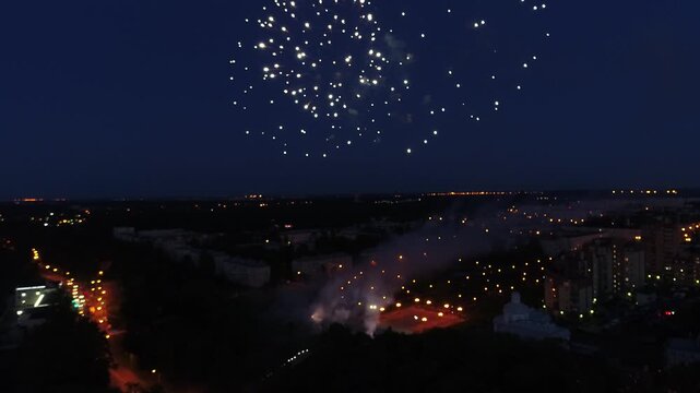 Aerial view of bright red fireworks exploding in the dark night sky over a city, with illuminated streets and buildings below