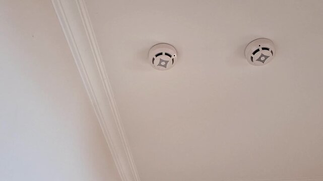 White smoke detectors mounted on a residential ceiling with crown molding trim, emphasizing interior safety features and home protection in a simple living space