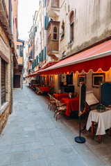 Naklejka premium Quiet street in Venice with empty tables and chairs under red awnings in the evening
