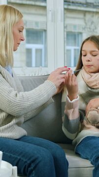 Cute sick 15-aged girl with scarf around neck sitting near caring mom and holding thermometer in the mouth because cought cold ,flu concept