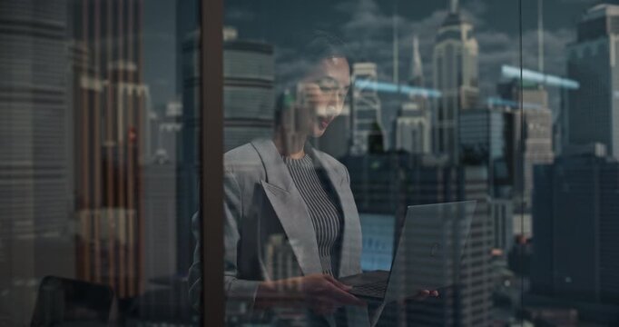 Smiling Portrait of Succesful Asian Businesswoman at a High-rise Window Looking the Financial District. Working on Her laptop. Creating Digital Software Startup and Finishing Fintech Project. 