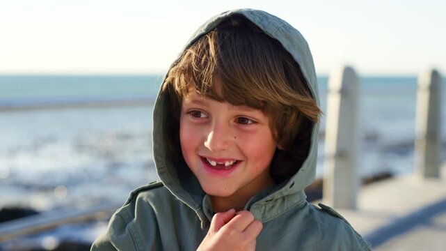 Smile, child and vacation by ocean, thinking and adventure on promenade outdoor with breeze. Sea, kid and boy with idea by coast for happiness, sightseeing and reflection on holiday with wind