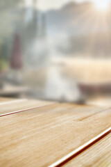 Empty wooden table with clear copy space for product placement, set outdoors during spring or summer. Blurred background of barbecue scene suggests grilling, outdoor dining and relaxation.
