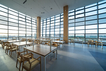 Naklejka premium Modern library reading room with empty wooden tables and chairs under large glass curtain walls