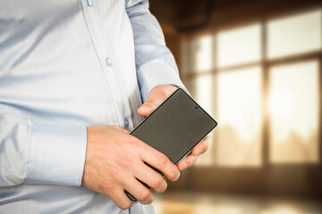 Businessman hands holding a smartphone, clean and neutral office background. Modern communication, digital business and mobile technology.