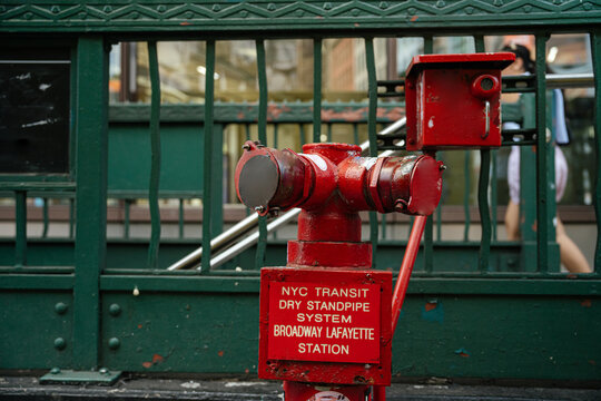 A red NYC Transit dry standpipe system stands outside the Broadway Lafayette subway station in New York City. The green metal entrance structure highlights the iconic urban transportation