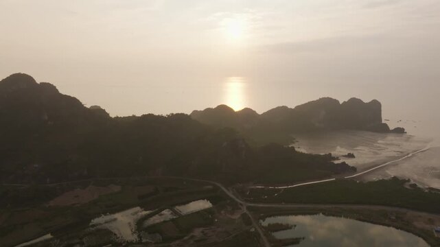 Cat Ba Vietnam aerial push toward limestone hills in silhouette, with wetlands and farmland textures in the foreground.