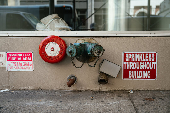 A red sprinkler fire alarm and standpipe connection are mounted on a building wall in New York City. Safety signage highlights fire protection infrastructure in an urban environment.