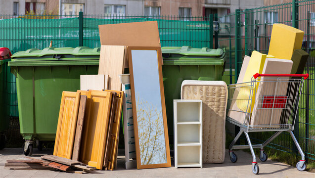 Old furniture and bulky household items stacked near outdoor trash bins for waste collection.