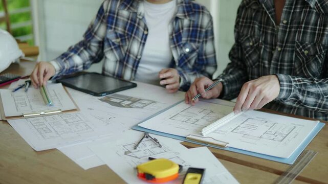 Architect and engineer working brainstorming and measuring for cost estimating on paperworks and floor plan drawings about design architectural and engineering for houses and buildings.