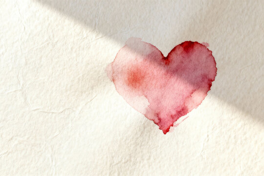 Red watercolor heart painted on textured handmade paper background, artistic romantic concept with natural sunlight shadows and copy space