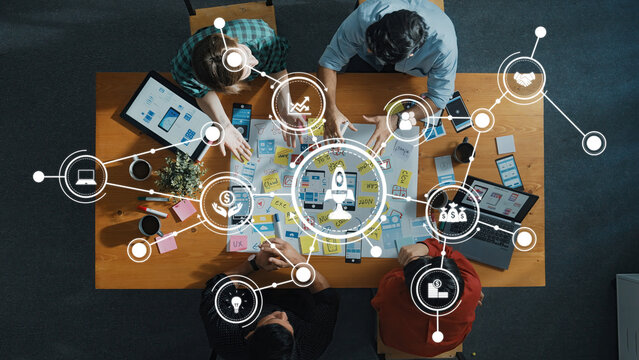 A top-down view of a business team collaborating on a digital strategy, surrounded by technology icons and data charts in a modern office setting, emphasizing teamwork and innovation. Amity