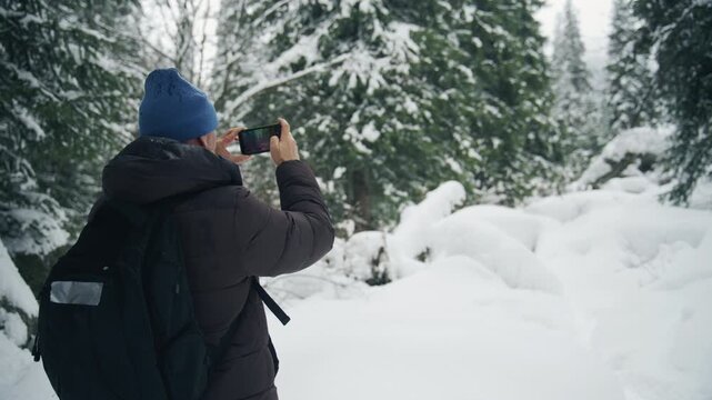 Hiker taking photo with smartphone in snowy winter forest