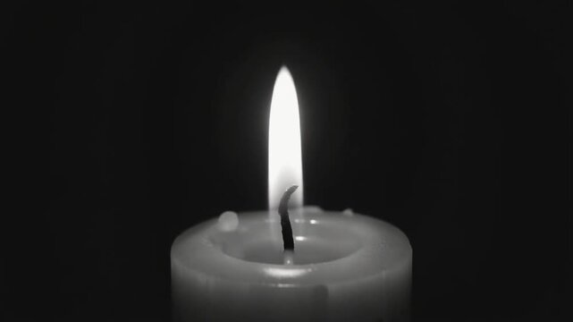 Close-up black and white image of a single lit candle with a bright flame on a dark background, symbolizing peace and remembrance