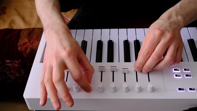 Close-up of music producer adjusting faders on MIDI controller, hands controlling sound in real time. Electronic music production, mixing and sound design in home studio using DAW