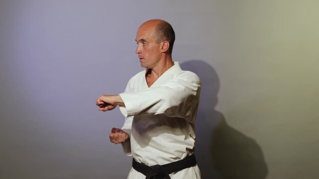 Against a light background, a young athlete with a black belt performs formal exercises
