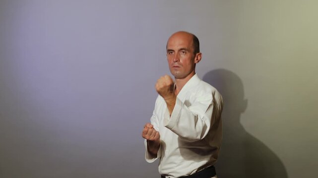 Against a light background, an athlete with a black belt practices hand strikes in a standing position while moving