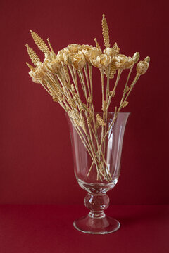 A glass vase with a bouquet of flowers made from straw on the red background. Straw weaving