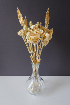 A glass vase with a bouquet of flowers made from straw on a gray background. Straw weaving