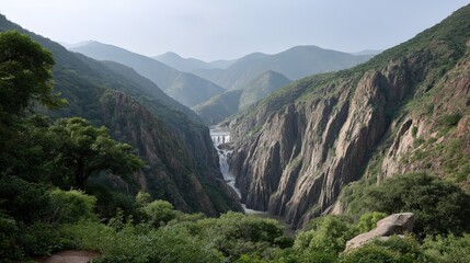 Obraz premium Water flows down rocks into a river while mountains and greenery fill the background under a clear sky. The scene shows nature's beauty