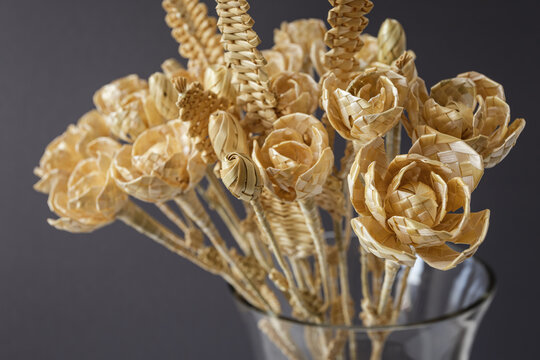 A glass vase with a bouquet of flowers made from straw on a gray background. Straw weaving