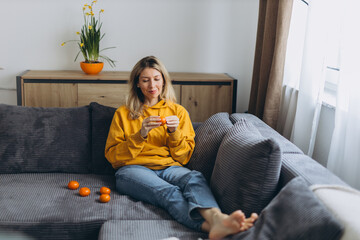 Fototapeta premium Woman peeling tangerine on sofa enjoying slow mindful routine and simple daily pleasure in cozy home lifestyle with soft light