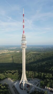 Vertical aerial orbiting shot of Avala tower with blue sky and green landscape, Belgrade, Serbia.