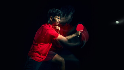 Fototapeta premium Table tennis player hitting powerful shot with strong motion effect in dark studio. Concept of physical strength expression, explosive energy, force application and high intensity sports performance.