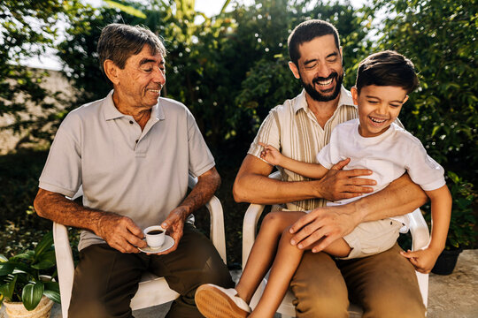Grandfather, adult son and young grandson sitting outdoors and interacting with affection, representing family bonding and multigenerational connection.