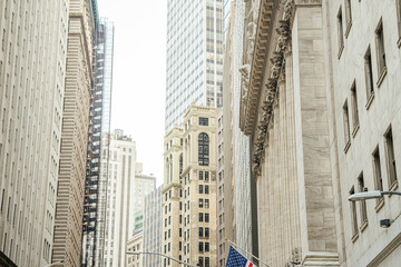 Tall skyscrapers and classic financial architecture rise above Wall Street in New York City. The financial district showcases corporate buildings, investment offices, and urban city infrastructure.