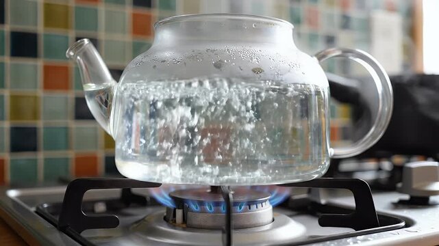 Glass teapot on a stovetop with boiling water, colorful tiled backsplash