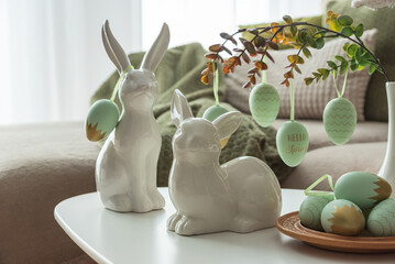 Obraz premium Cozy Easter Living Room Decor with Bunny Figurines and Hanging Eggs on White Table