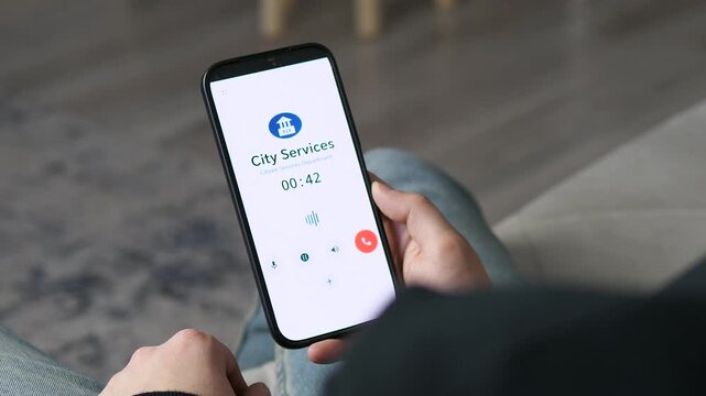 Close-up of male hands holding a smartphone during an active call with municipal services. The screen shows the call in progress. Great for customer support, civic engagement, or help desk themes.