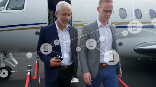 Animation of network of digital icons over two caucasian businessmen walking at airport