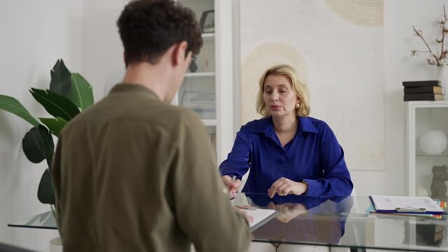 Young man signing divorce papers while lawyer explains details in office