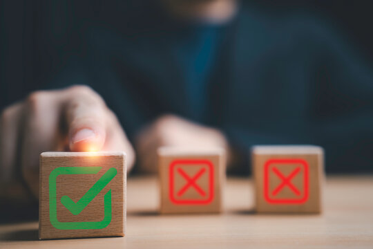 Hand selecting green checkmark on wooden block while rejecting incorrect options. Concept of decision making, quality control, approval process, business validation and risk management strategy.