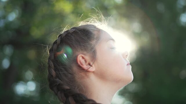 Girl breathing in sunlight profile face lifted eyes closed child with braid braided hair lit by sunflare tree bokeh around relaxed expression outdoor nature portrait evoking calm and simplicity