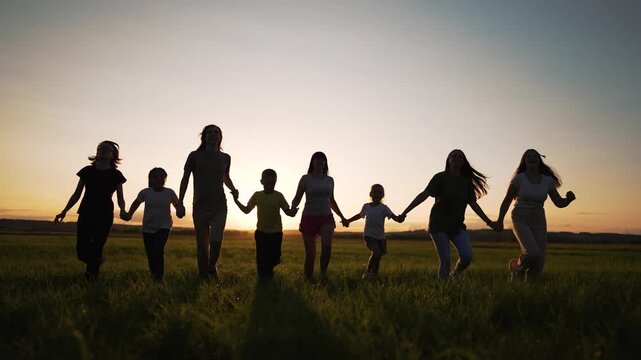 Running hand in hand across field at sunset silhouette of family and child hold hands in tall grass as group share friendship together and appear happy under warm golden sky sharing family bond
