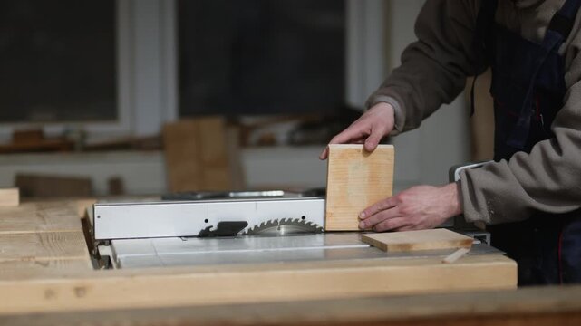 A skilled woodworker wearing protective gear carefully positions a piece of wood on a powerful table saw. The craftsman is focused on the precision cutting task in his professional workshop.