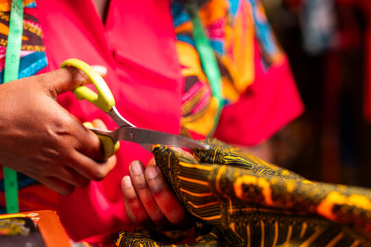 African tailor's hands cutting colorful wax print fabric with scissors in a sewing workshop