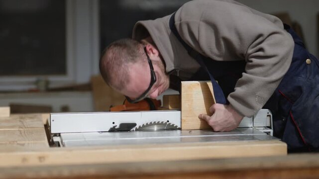 A craftsman wearing safety glasses carefully positions wood on a table saw. He meticulously prepares for a precise cut in his workshop.