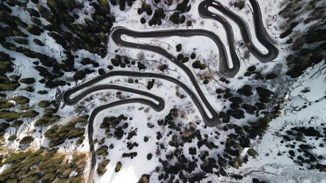 Top-down aerial view of a serpentine road winding through a snowy mountain range.
